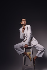 stylish young woman in white suit sitting on chair on dark background