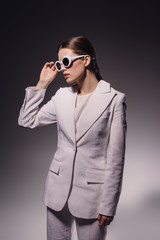 portrait of stylish woman in white suit and eyeglasses posing on dark backdrop