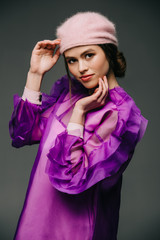 portrait of beautiful woman in fashionable purple dress and hat looking at camera on black background