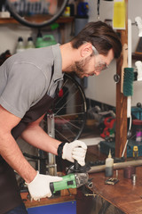 side view of young repairman in protective workwear holding angle grinder in workshop