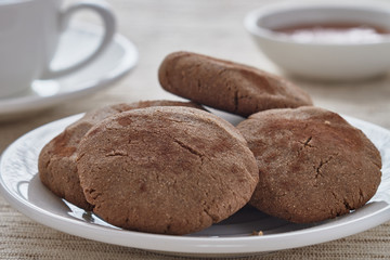 Homemade biscuits of buckwheat flour with honey on a plate and a cup of coffee on a wooden background.