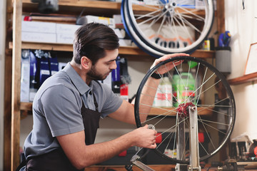 Obraz na płótnie Canvas young man in apron repairing bicycle wheel in workshop
