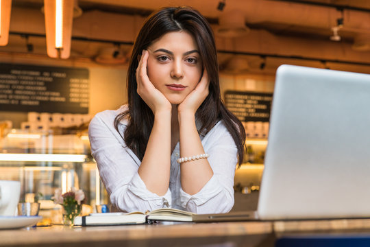 Portrait of young businesswoman, student, dressed in white blouse, sitting at table in cafe in front of computer.