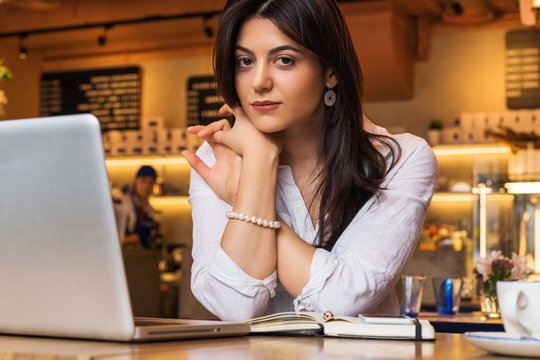 Portrait of young businesswoman. Girl works remotely on laptop in restaurant. Online marketing, education, e-learning.