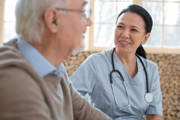 My patient. Appealing happy doctor wearing uniform while gazing at senior man and smiling