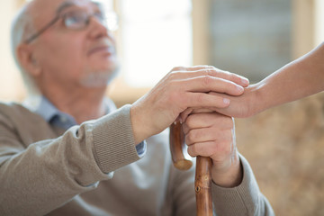 My gratitude. Selective focus of wooden cane and senior male hands holding it and putting other...