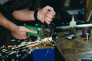 close-up partial view of man cutting metal with angle grinder in workshop