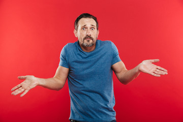 Portrait of caucasian adult man looking at camera expressing misunderstanding with throwing up...