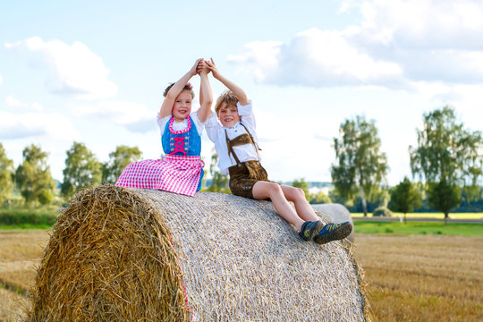 Two kids, boy and girl in traditional Bavarian costumes in wheat field with hay bales
