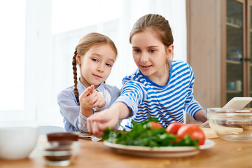 Waist up portrait of two girls cooking in kitchen, elder sister teaching little one, copy space