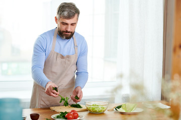 Waist up portrait of handsome mature man cooking salad in spacious kitchen at home, copy space