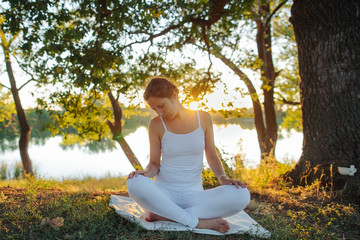 young yogin girl sits in a meditative position on the picturesque shore of the lake