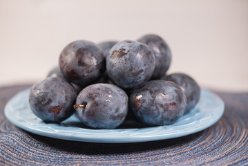 Fresh ripe blue plums on plate, wooden table with napkin