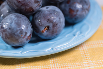 Fresh ripe blue plums on plate, wooden table with napkin