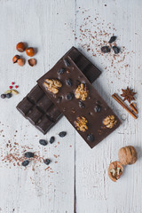 two chocolate bar filled with different berries and nuts lie old wooden table with cracked paint on the surface.scattered Almonds, nuts,buckwheat, and grated cinnamon.  strongly blurred background