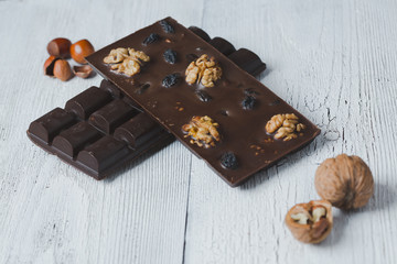 two chocolate bar filled with different berries and nuts lie old wooden table with cracked paint on the surface.scattered Almonds, nuts,buckwheat, and grated cinnamon.  strongly blurred background