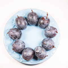 Fresh ripe blue plums on plate, wooden table