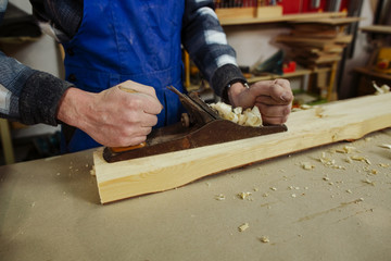 The woodworker keeps in the hands of the plane, which stands on a timber bar and is ready for work. Scraping the bar