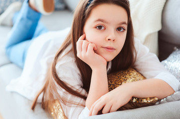 happy kid girl close up portrait. Preteen relaxing at home on cozy couch in white shirt and casual jeans. Happy childhood.