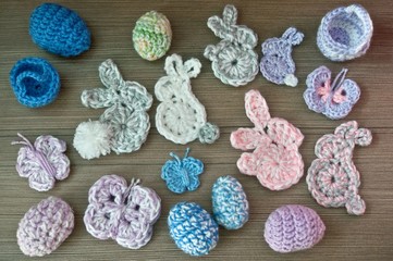 Easter decoration, bunny rabbits, butterflies, eggs, baskets, made of crochet colorful yarn on wooden texture background. Homemade decor. Top view, shallow depth of focus. Easter holidays.