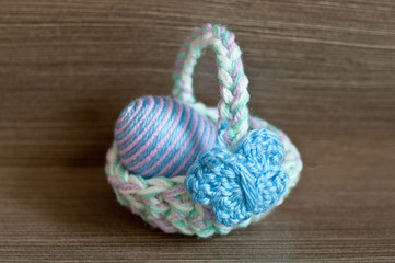 Obraz na płótnie Canvas Easter decoration, crochet mini basket, striped colorful egg wrapped in soft yarn thread, pastel colors, butterfly, wooden texture background. Homemade decor. Shallow depth of focus. Easter holidays.
