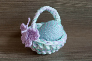 Fototapeta na wymiar Easter decoration, crochet mini basket, striped colorful egg wrapped in soft yarn thread, pastel colors, butterfly, wooden texture background. Homemade decor. Shallow depth of focus. Easter holidays.