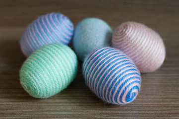 Easter decoration, colorful striped eggs wrapped with soft yarn thread on wooden texture background. Pastel green blue violet pink beige colors. Homemade decor. Shallow depth of focus. Easter holidays
