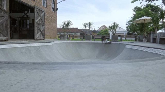 Young man skating in concrete skatepark bowl and then jumping out on skateboard and riding towards the camera