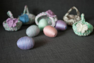 Easter decoration, crochet basket, striped colorful egg wrapped in soft yarn thread, pastel colors, butterfly, dark grey texture background. Homemade decor. Shallow depth of focus. Easter holidays.