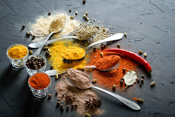 Various spices(pepper ground turmeric ginger cinnamon grass seasoning) in metal antique spoons on stone beton table. Top view