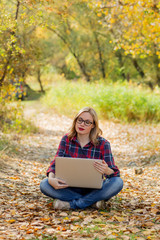 A girl with a laptop on her lap, closing her eyes, resting in an autumn park.