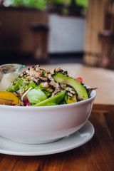 Green salad poke bowl with sesame dressing on a wooden table. Vegetarian raw meal concept