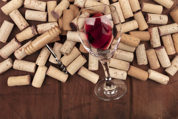 Glass of red wine with corks and corkscrew on a dark rustic background with copy space