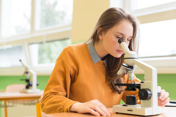 High School female student in biology class. Student using microscope to examine samples.