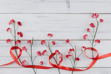 Red paper flowers with branch and red ribbon on white wood background with copy space