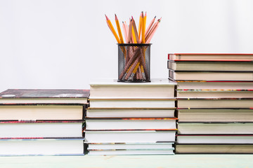 Set of pencils and pile of various books on wooden background. With copy space for your text