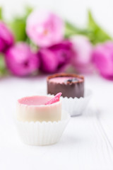 Hand made chocolate candies and pink tulips on a white background. Free space