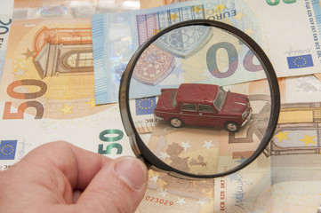 billetes de euro con coche mirado con lupa