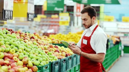 Serious seller consultant using digital tablet in supermarket near fruit worker internet communication man holding connection job organic market store stand tablet pc shop touch business staff - Powered by Adobe