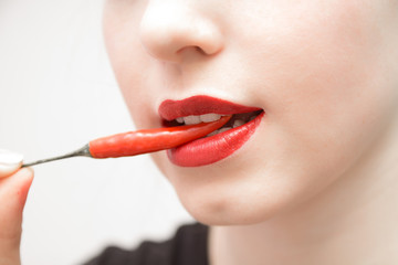 woman's mouth with red lips opened  and white teeth holding a red chilli pepper