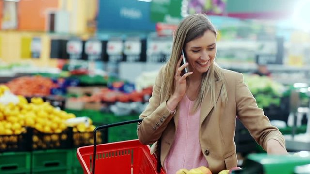 Attractive young woman talking on phone smiling chooses apples and puts in basket in supermarket mall cellphone casual shopper copy lady fashion food girl shopping fruit market buy store cell happy
