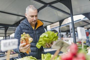 Fototapeta premium Mature man picking vegetables at farmers's market. Man buying organic fruits and vegetables at an open street market. Local Farmers Market. Fresh produce: vegetables