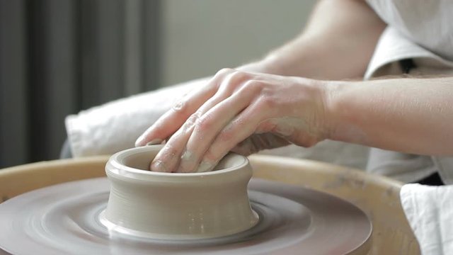 Process of creating dishes on a rotating potter's wheel by hand. Close-up mens hands of the master are quickly shaped into bowls of clay mass and water.