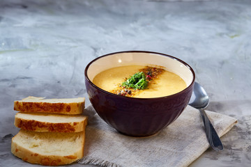 Porcelain bowl of pumpkin soup on napkin over white textured background, close-up, selective focus, top view.