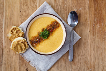 Ceramic bowl of pumpkin soup on napkin over rustic wooden background, close-up, selective focus, top view.
