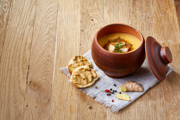 Clay pot of pumpkin soup on homespun napkin rustic wooden background, close-up, selective focus, top view.