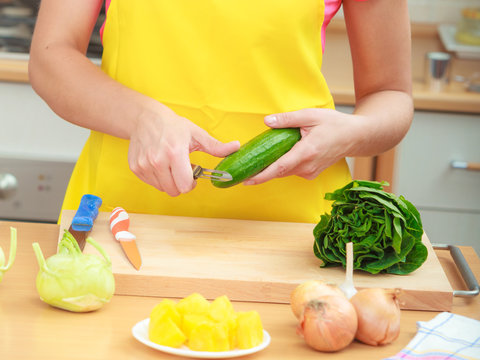 Woman preparing vegetables salad peeling cucumber