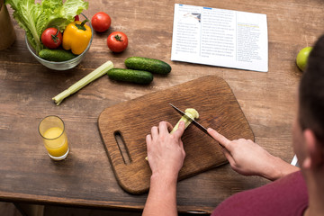 cropped shot of young man cutting celery on wooden chopping board