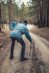 An elderly man walking along a road in a pine forest