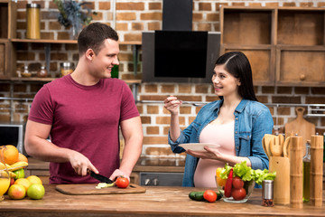 happy young pregnant couple smiling each other while cooking together